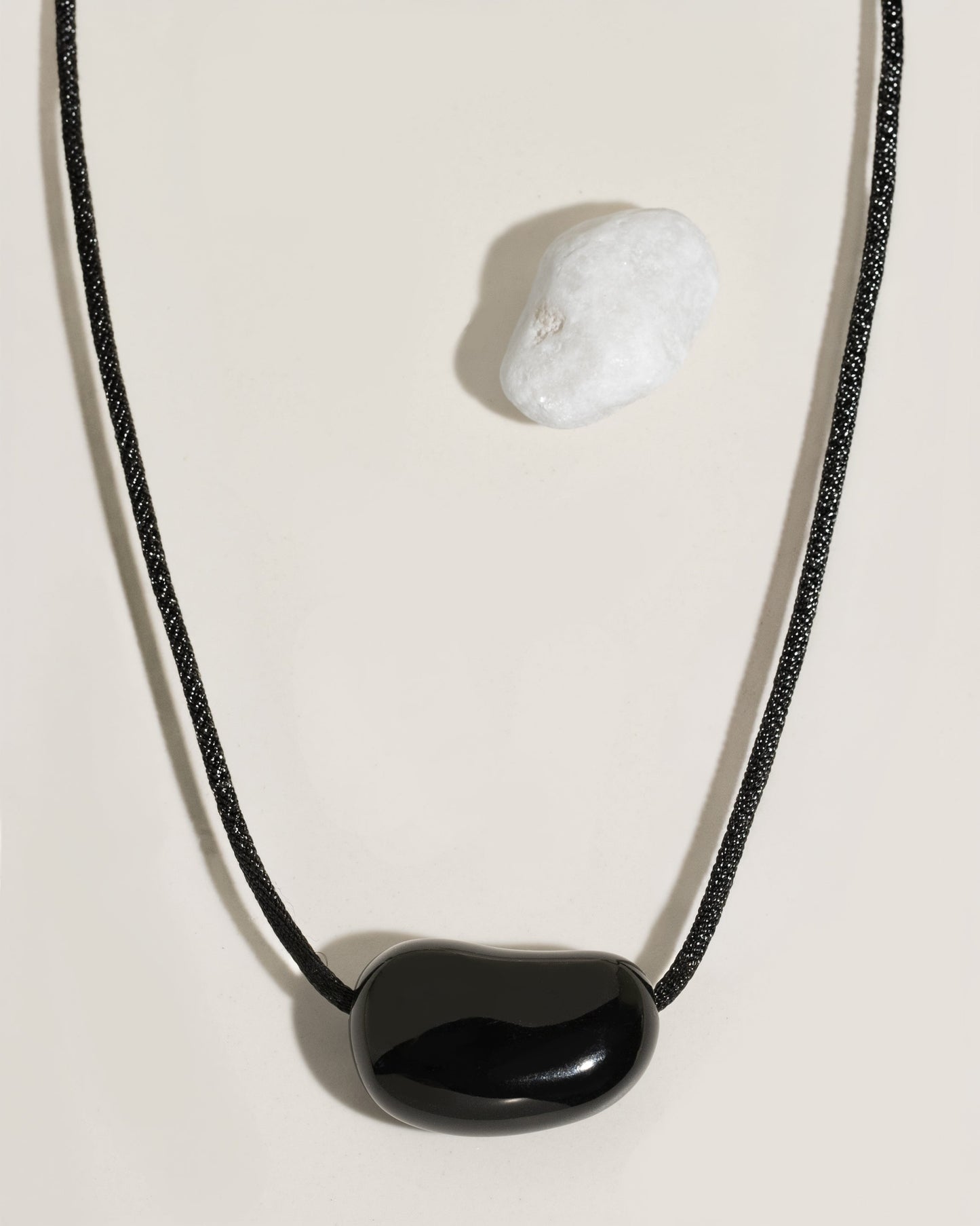 Black cord necklace with a polished black organic-shaped stone pendant on cream surface