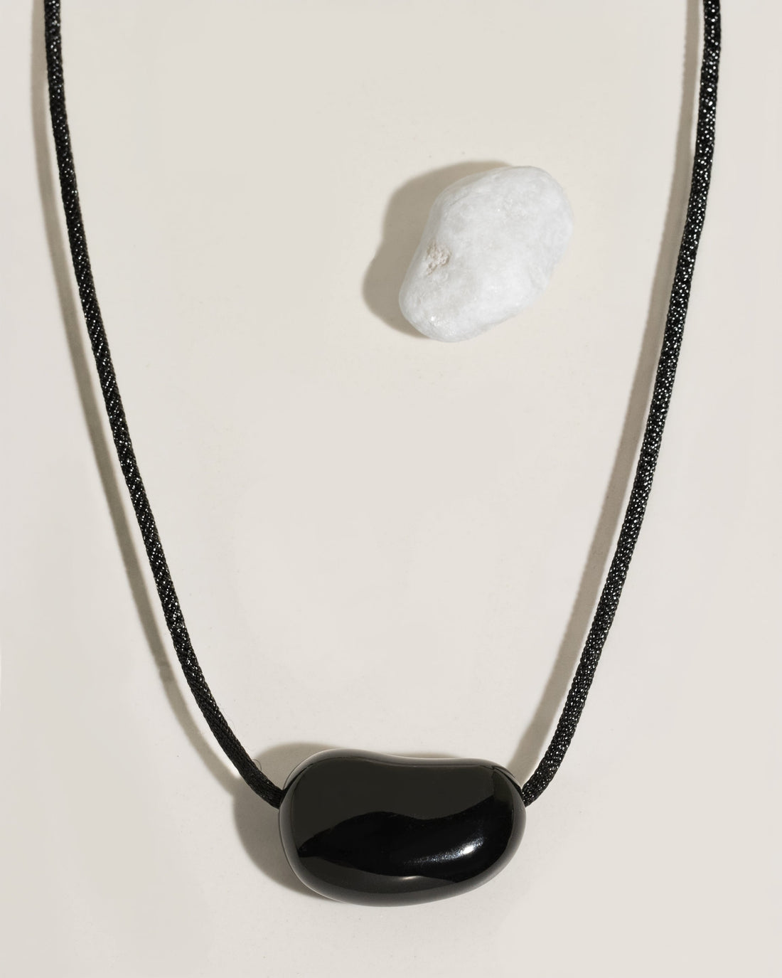 Black cord necklace with a polished black organic-shaped stone pendant on cream surface