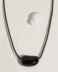 Black cord necklace with a polished black organic-shaped stone pendant on cream surface