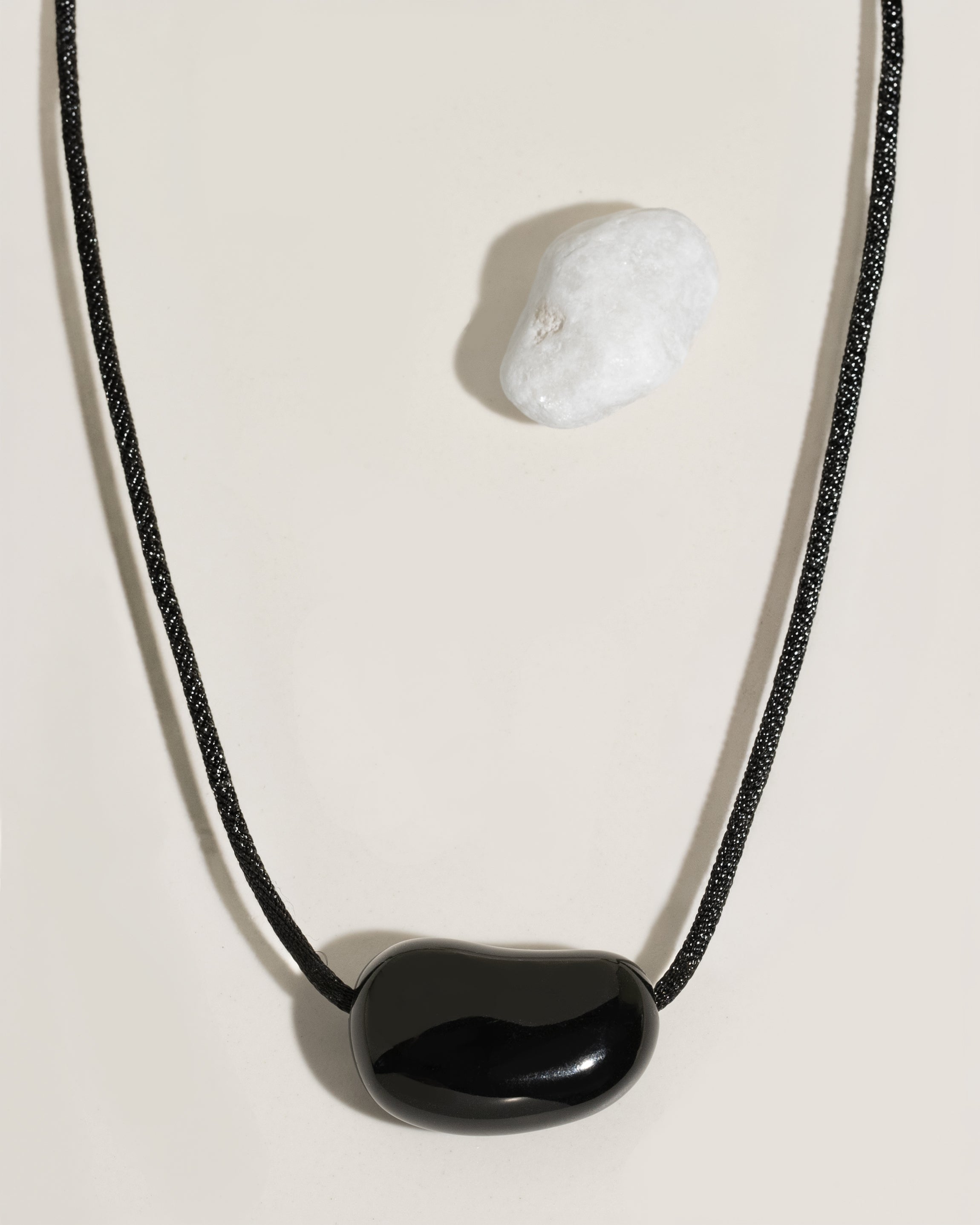 Black cord necklace with a polished black organic-shaped stone pendant on cream surface