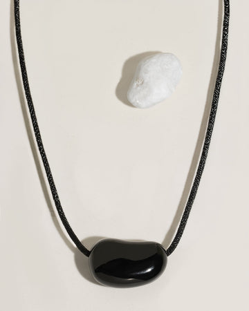 Black cord necklace with a polished black organic-shaped stone pendant on cream surface