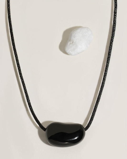 Black cord necklace with a polished black organic-shaped stone pendant on cream surface